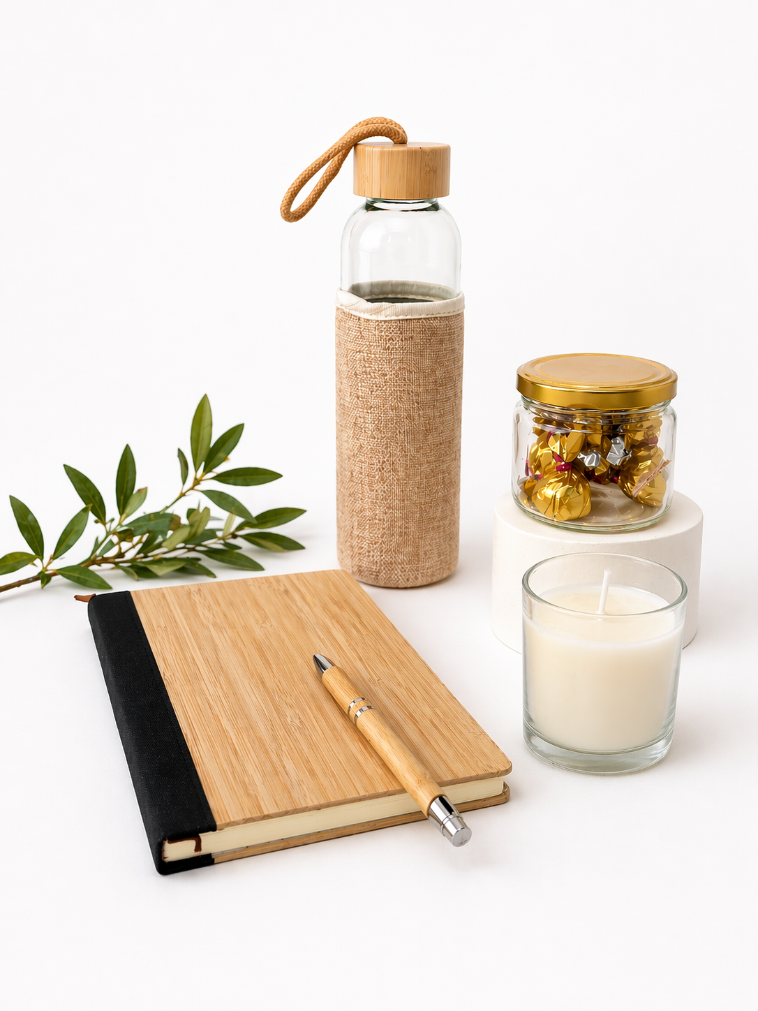 Set of eco-friendly items including a glass water bottle with bamboo cap, notebook, pen, candle, and jar